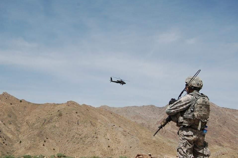 Service member watching a helicopter over mountain terrain